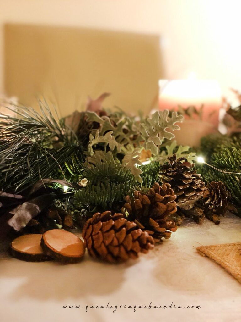 Decoracion Mesa Navidad compuesta por diferentes ramas verdes, velas, piñas, y más elementos decorativos.