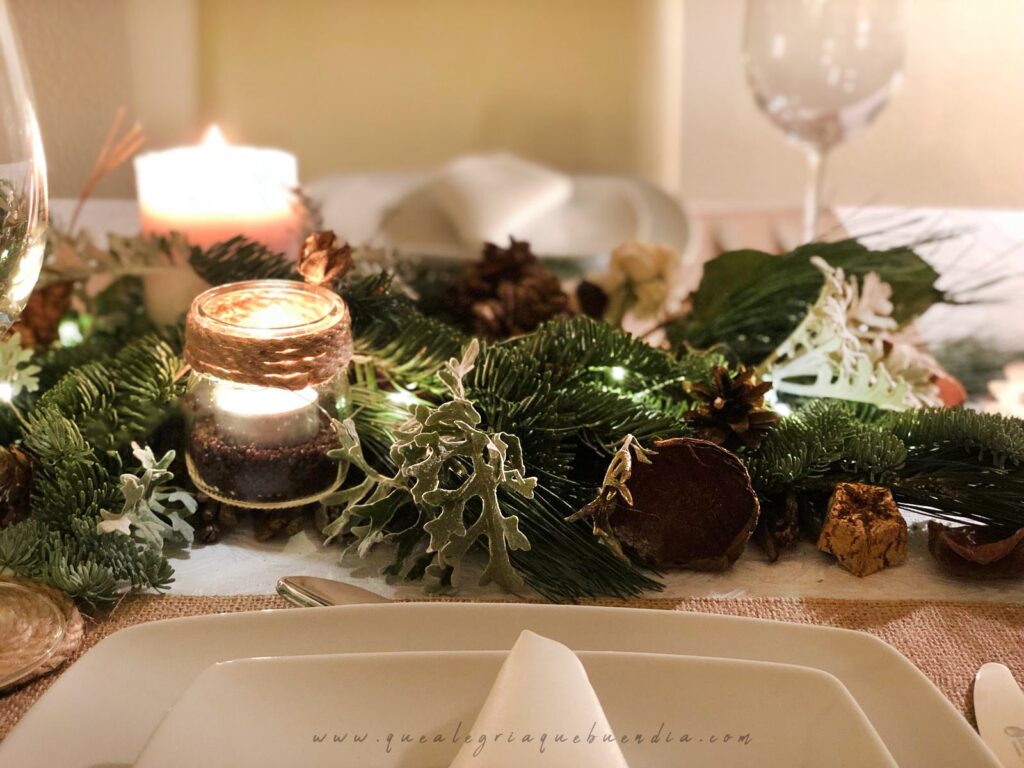 Decoracion Mesa Navidad compuesta por diferentes ramas verdes, velas, piñas, y más elementos decorativos.