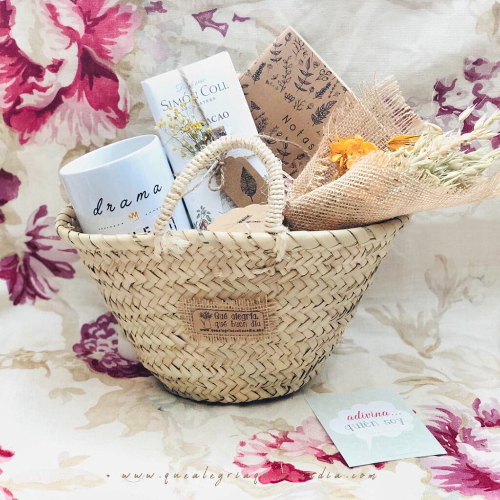 MiniPack Capazo regalo ideal para el amigo invisible. Esta compuesto por capazo de mimbre, taza, chocolate, libreta y ramo de flores. Regalos hechos a mano